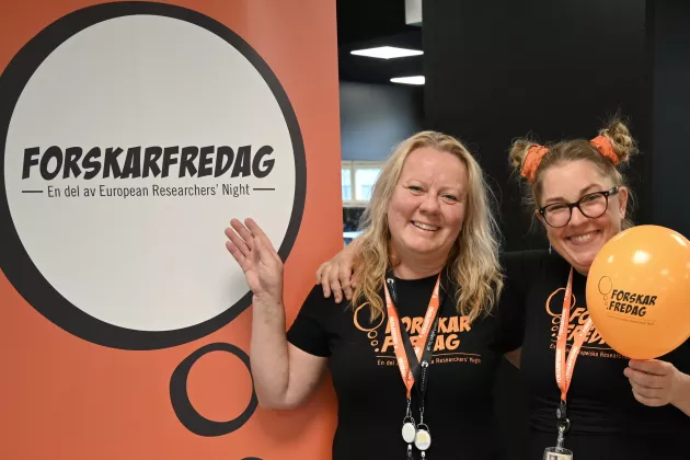 Två kvinnliga forskare som står med ballonger framför en skylt med rubriken ForskarFredag.